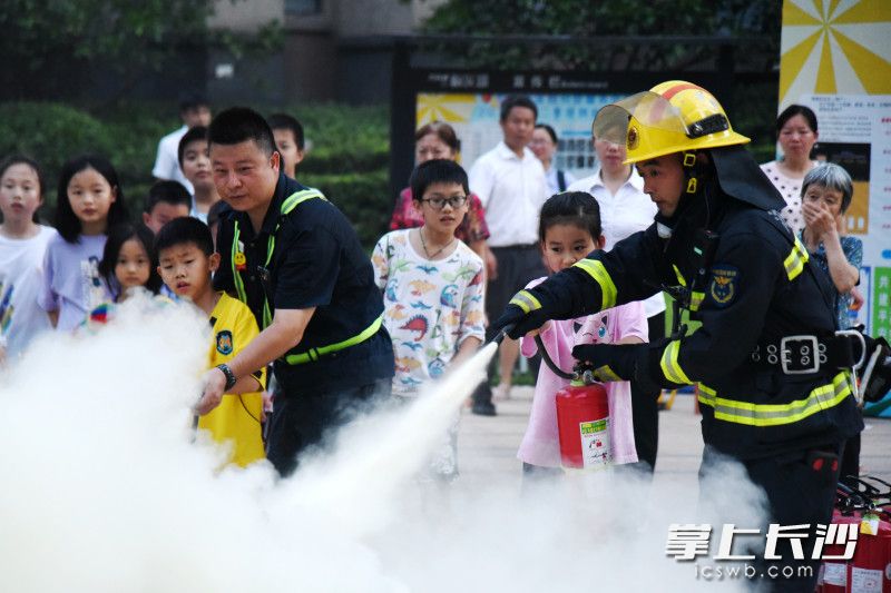 在“火焰蓝”和物业人员的带领下，中小学生上前体验用干粉灭火器灭火。