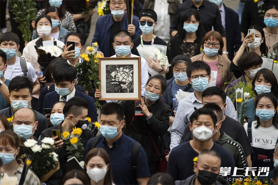 5月24日，一位手举着袁老剪纸的市民排队进入殡仪馆缅怀袁老。