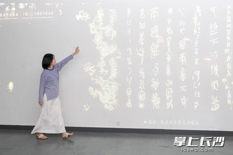 一位游客伸手掠过《溯源书法文脉，推进文化自信——中国简帛书法艺术临摹创作光影展》屏幕，屏幕文字随即产生交互，飞散飘扬，十分生动。