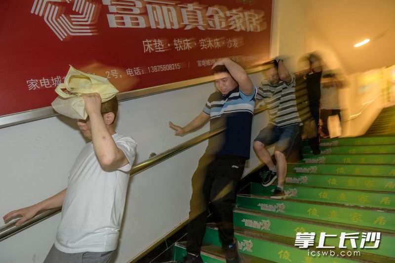 地震紧急疏散演练现场，伴随着尖利的警报声响起，三湘大市场家电城放心购物街内的数十位居民群众立刻有序地护头沿着扶梯下楼撤离。长沙晚报全媒体记者 陈飞 摄